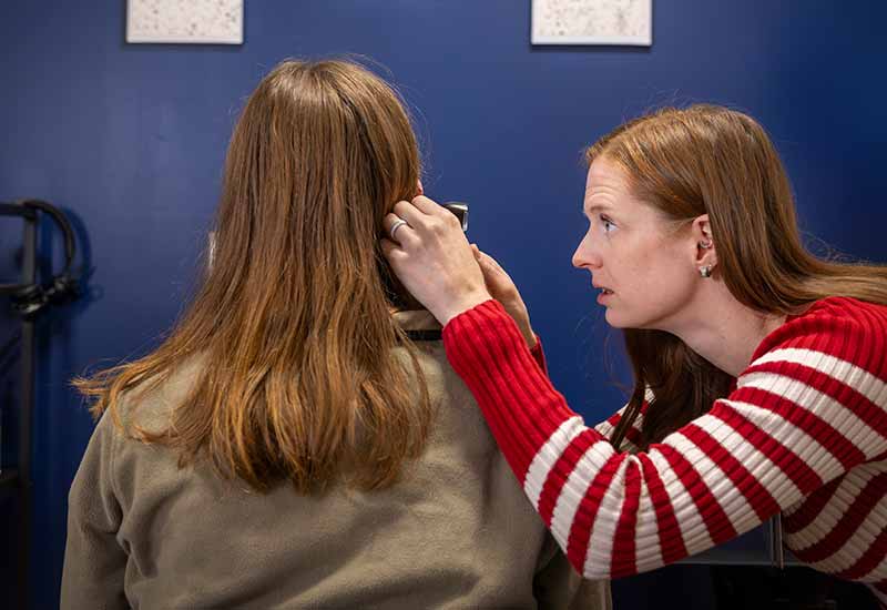 An audiologist uses an otoscope to performs a visual inspection of a patient's outer ear.