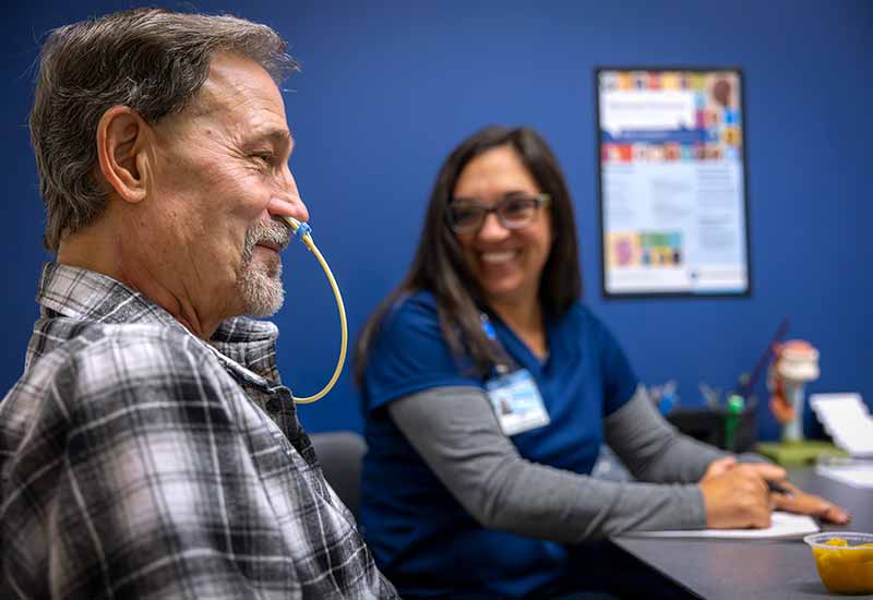 A speech-language pathologist is completing a dysphagia (swallowing) evaluation on a patient with a feeding tube in place after a surgical procedure.