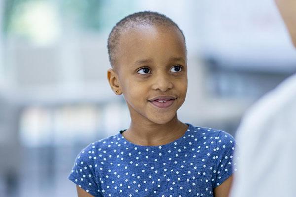 A female doctor and cancer patient are indoors in a hospital room. The girl is smiling. The doctor is telling the girl about her checkup.
