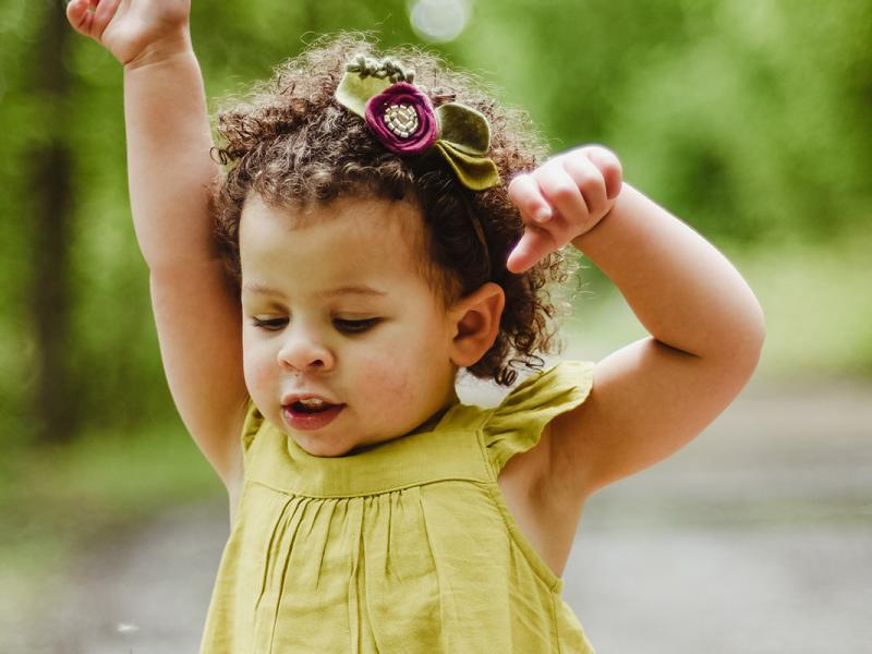 Girl in green dress plays outside surrounded by trees