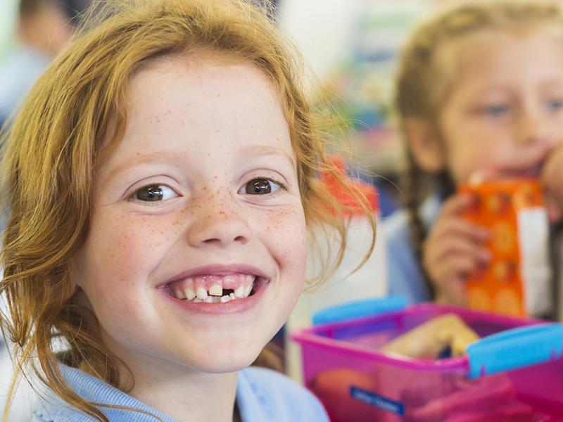 Smiling school students in uniform missing a tooth with a healthy sandwich for lunch
