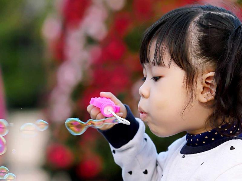 Toddler Girl Wearing White and Black Sweater Holding Plastic Bottle of Bubbles at Daytime