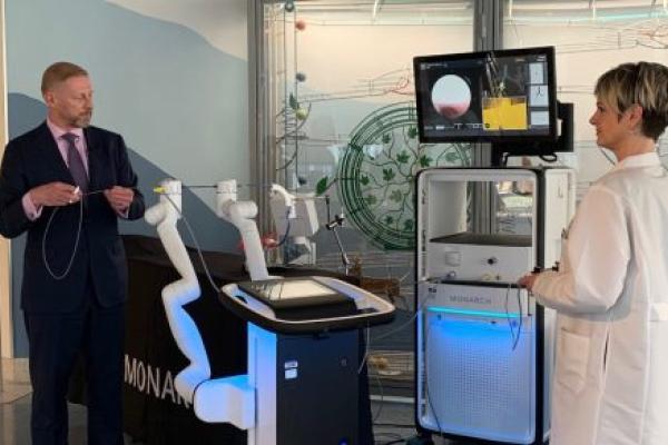 A man and a woman stand next to a robotic bronchoscopy too to demonstrate how it works.