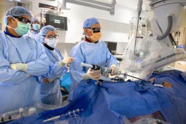 A medical team in full surgical attire, including masks, gowns, gloves, and protective eyewear, perform a procedure in a high-tech operating room.