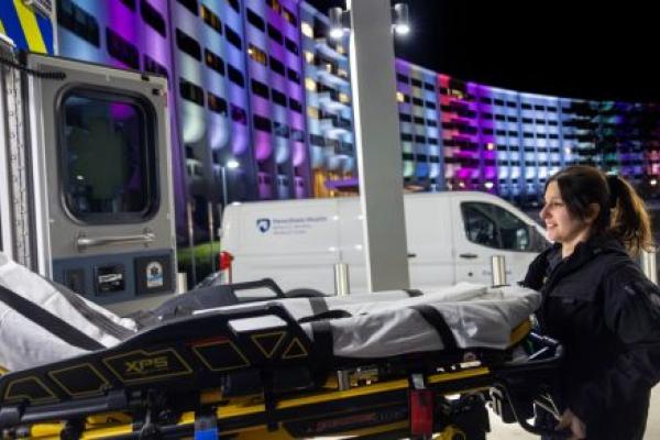 A Life Lion paramedic smiles while loading a stretcher into an ambulance outside Penn State Health Milton S. Hershey Medical Center at night.