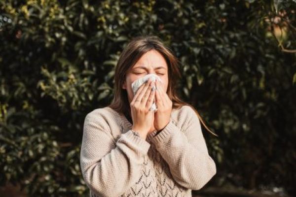 Young woman suffering spring allergy and blowing nose with a tissue.