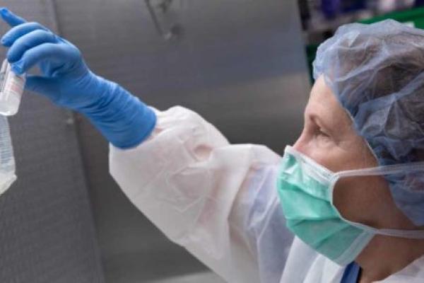 Un técnico de farmacia enmascarado que usa varios artículos de equipo de protección personal prepara remdesivir para un paciente en la farmacia.