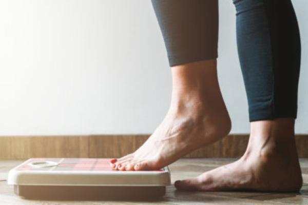 A woman steps onto a bathroom scale with her left foot first. Image is from the knees down.