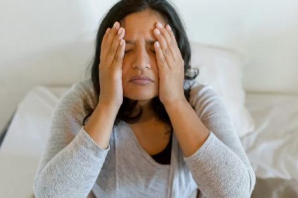 A woman rubs her head as she sits up in bed.