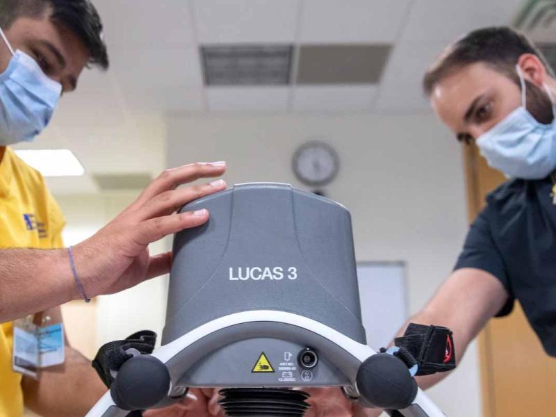 Steven Rodriguez, right, a nurse practitioner at Penn State Health, wearing navy blue scrubs, demonstrates a CPR machine to Harsh Bhohani, a nursing student wearing yellow scrubs, during a code blue simulation.