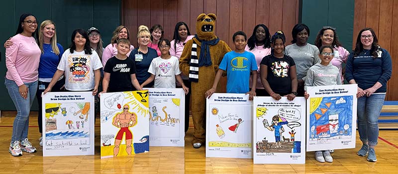 The six student finalists are standing holding their poster. Members of the Penn State Health Dermatology Clinic, Community Service Committee are standing behind them.