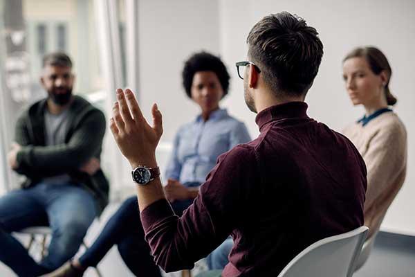 Rear view of man with raised hand on group therapy in a medical center setting.
