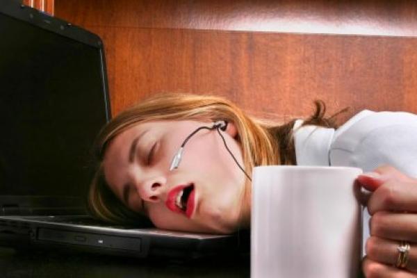 A woman sleeps on her laptop with her hand still holding her coffee.