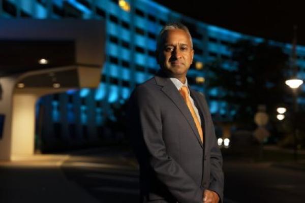 A man poses for a portrait in front of a building. The building is illuminated in blue lights.