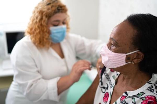 One masked woman provides another masked woman with a vaccine in her right arm.