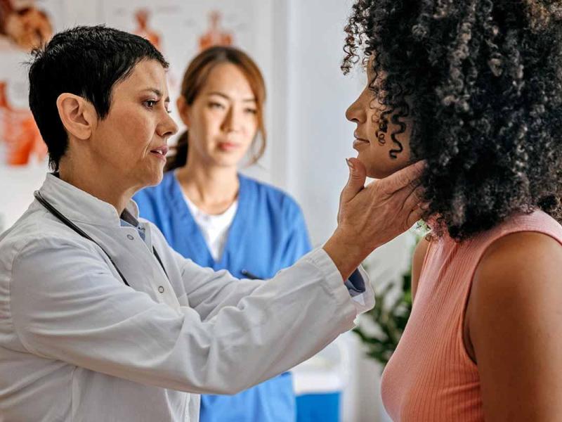 A female doctor examines a female patient in a medical office while a female nurse writes information about patient.