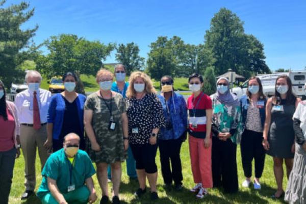 A group of 13 people stand outside on a lawn for a group photo