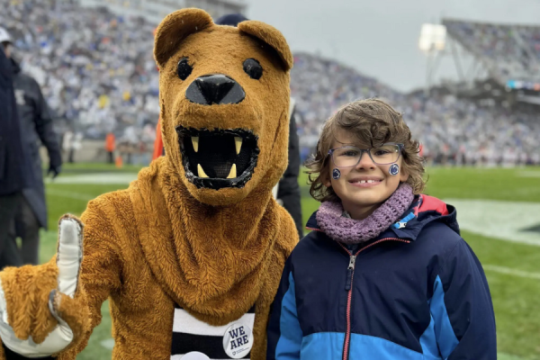 Young girl posing with the Penn State Nittany Lion on a football field.