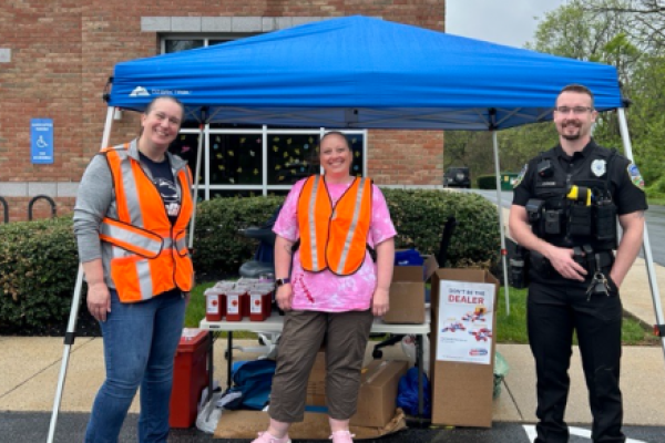 Two colleagues and a police officer stand with collection boxes and sharps containers outside a medical practice.
