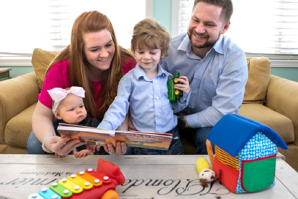 A family of four looks down at a book from the couch where they're sitting