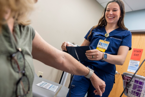 A medical professional in blue scrubs wraps a blood pressure sleeve around a patient's arm