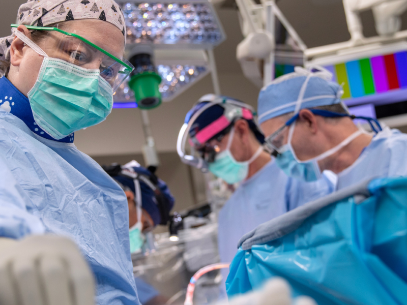 A cardiac surgical team performing complex heart surgery at Penn State Health. Surgeons and nurses dressed in light blue scrubs collaborate in a high-tech operating room.